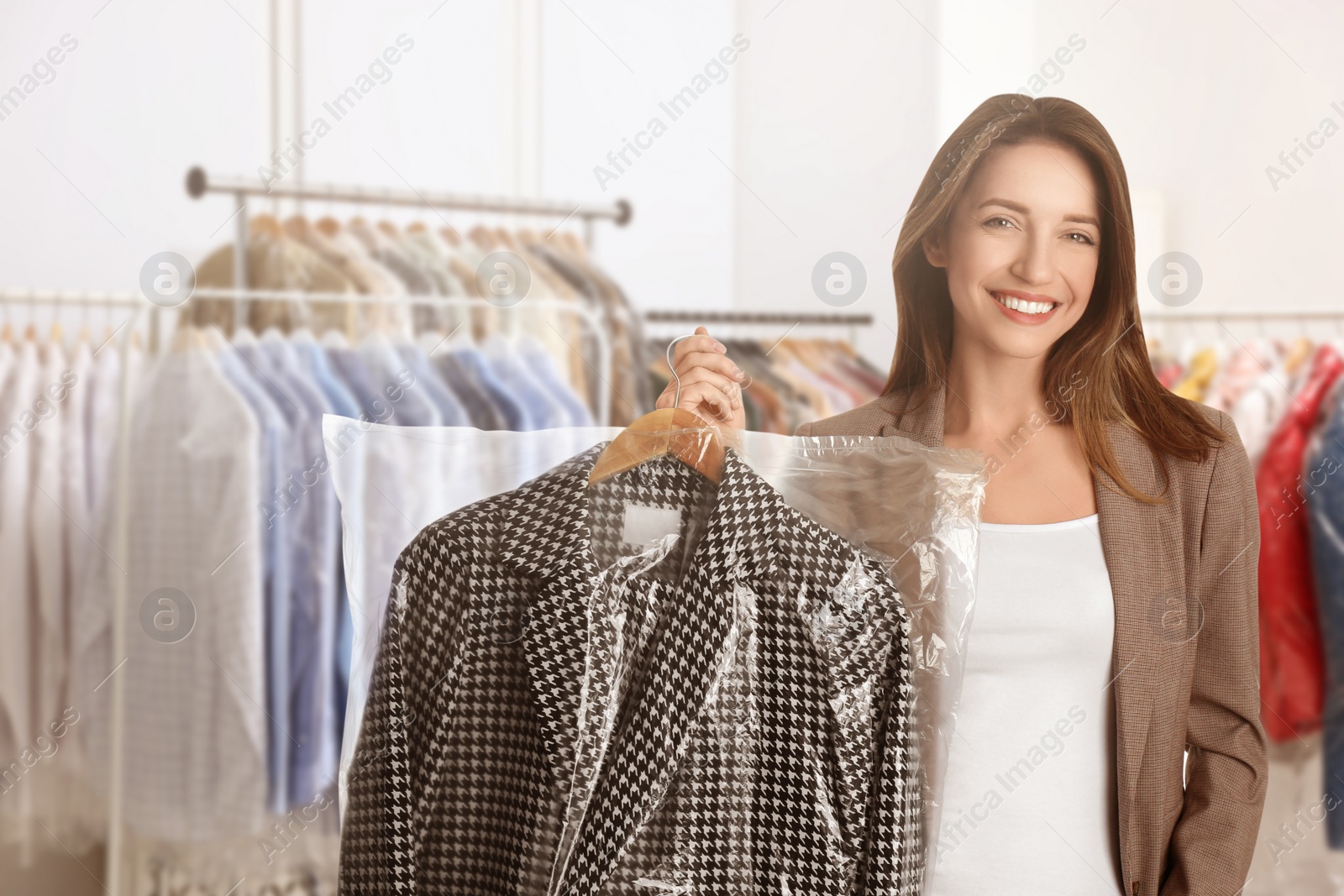 Image of Dry-cleaning service. Happy woman holding hanger with coat in plastic bag indoors