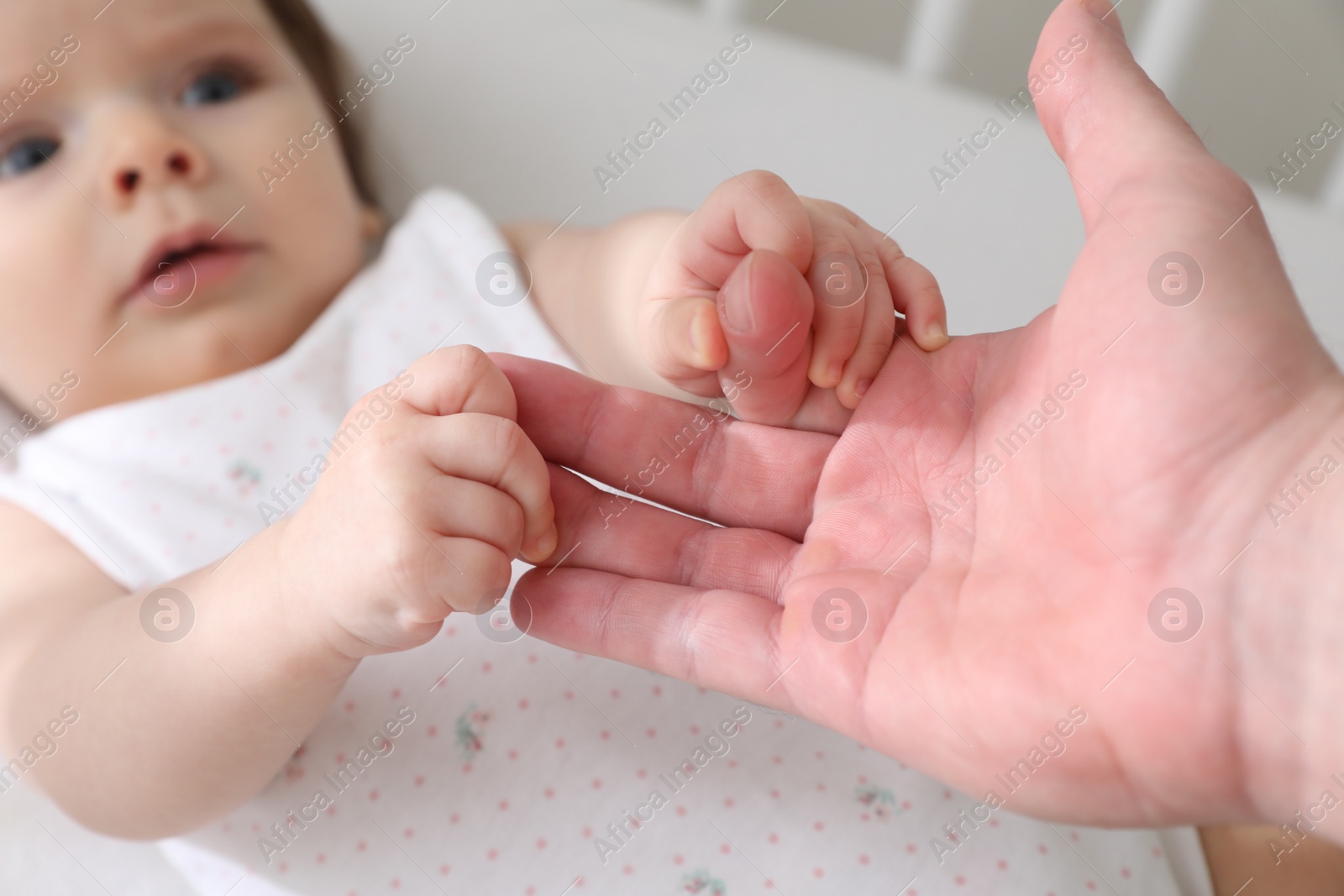 Photo of Father holding baby's hands in crib at home, closeup