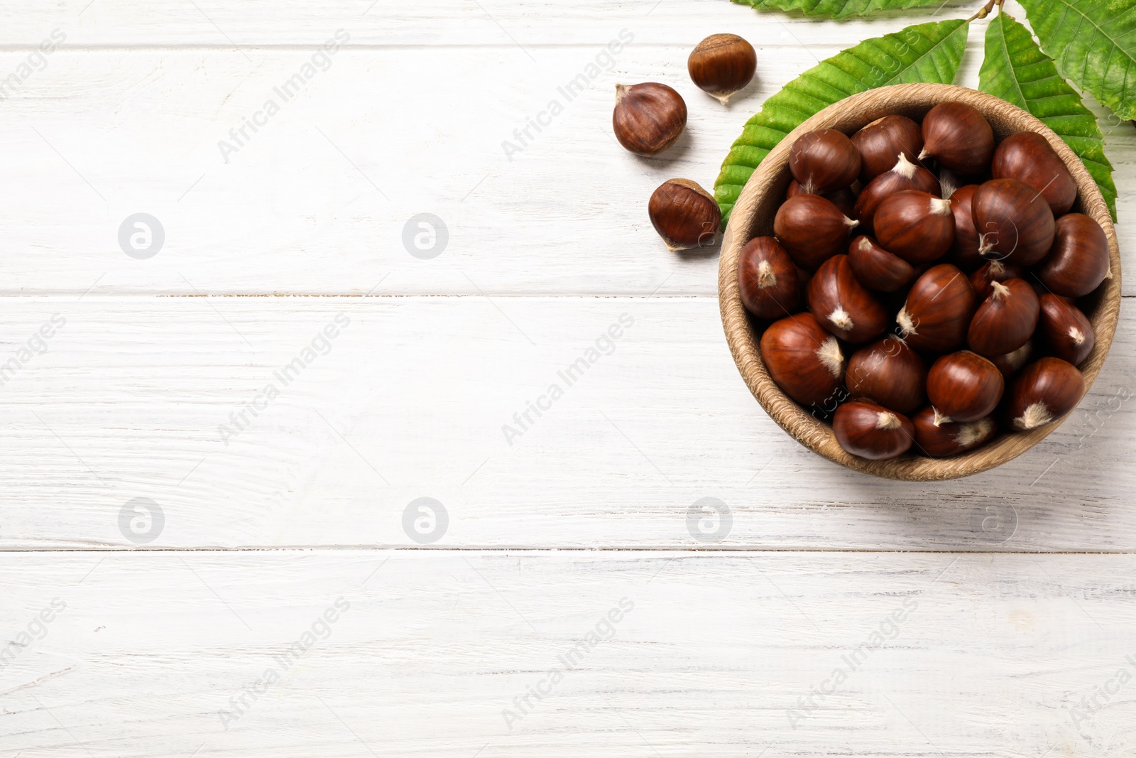 Photo of Fresh sweet edible chestnuts on white wooden table, flat lay. Space for text