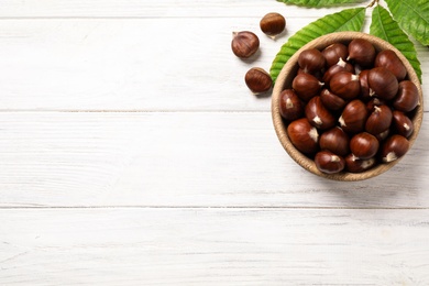 Fresh sweet edible chestnuts on white wooden table, flat lay. Space for text