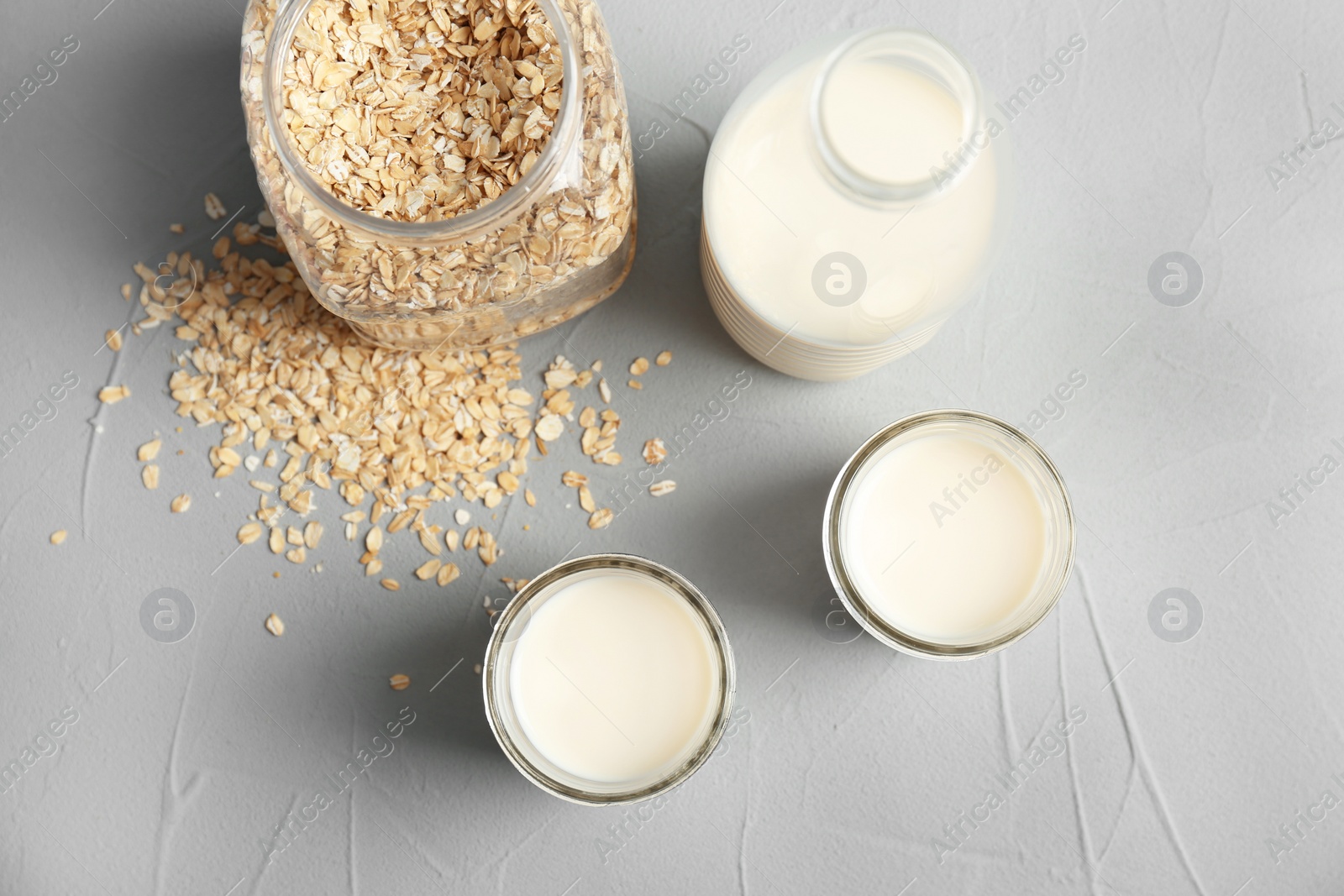 Photo of Jars with oat milk and flakes on grey background, top view