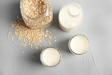 Photo of Jars with oat milk and flakes on grey background, top view