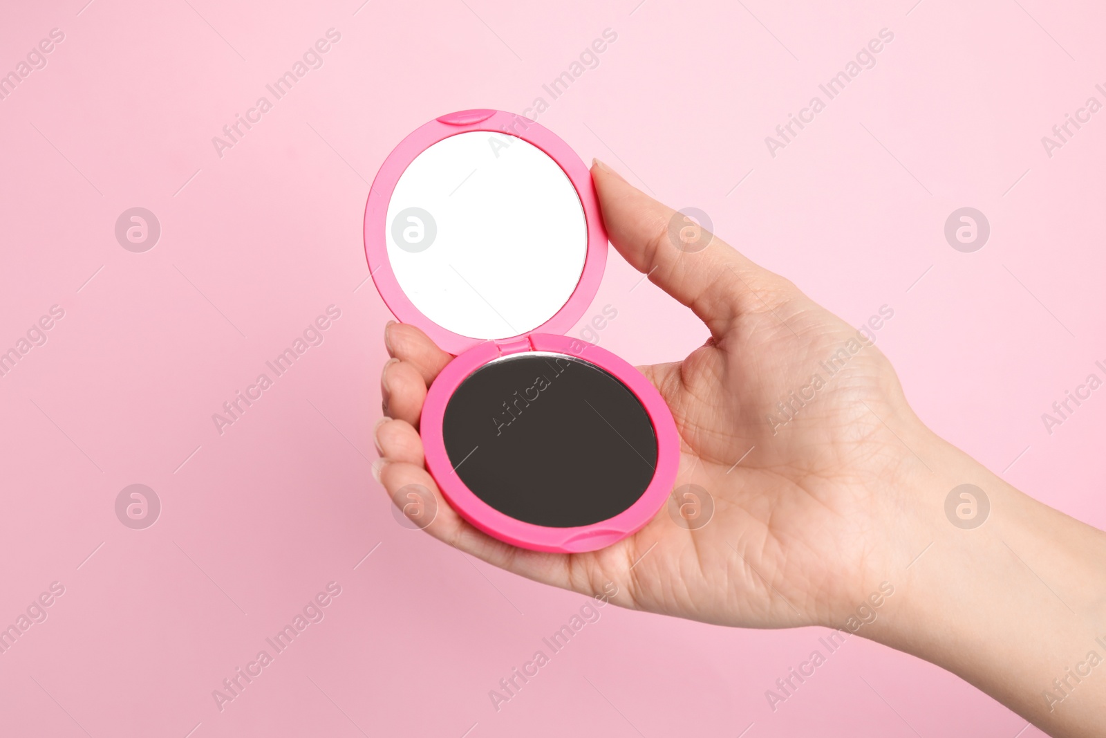 Photo of Woman holding stylish cosmetic pocket mirror on pink background, closeup