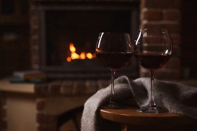 Photo of Glasses of red wine on wooden table near fireplace. Space for text