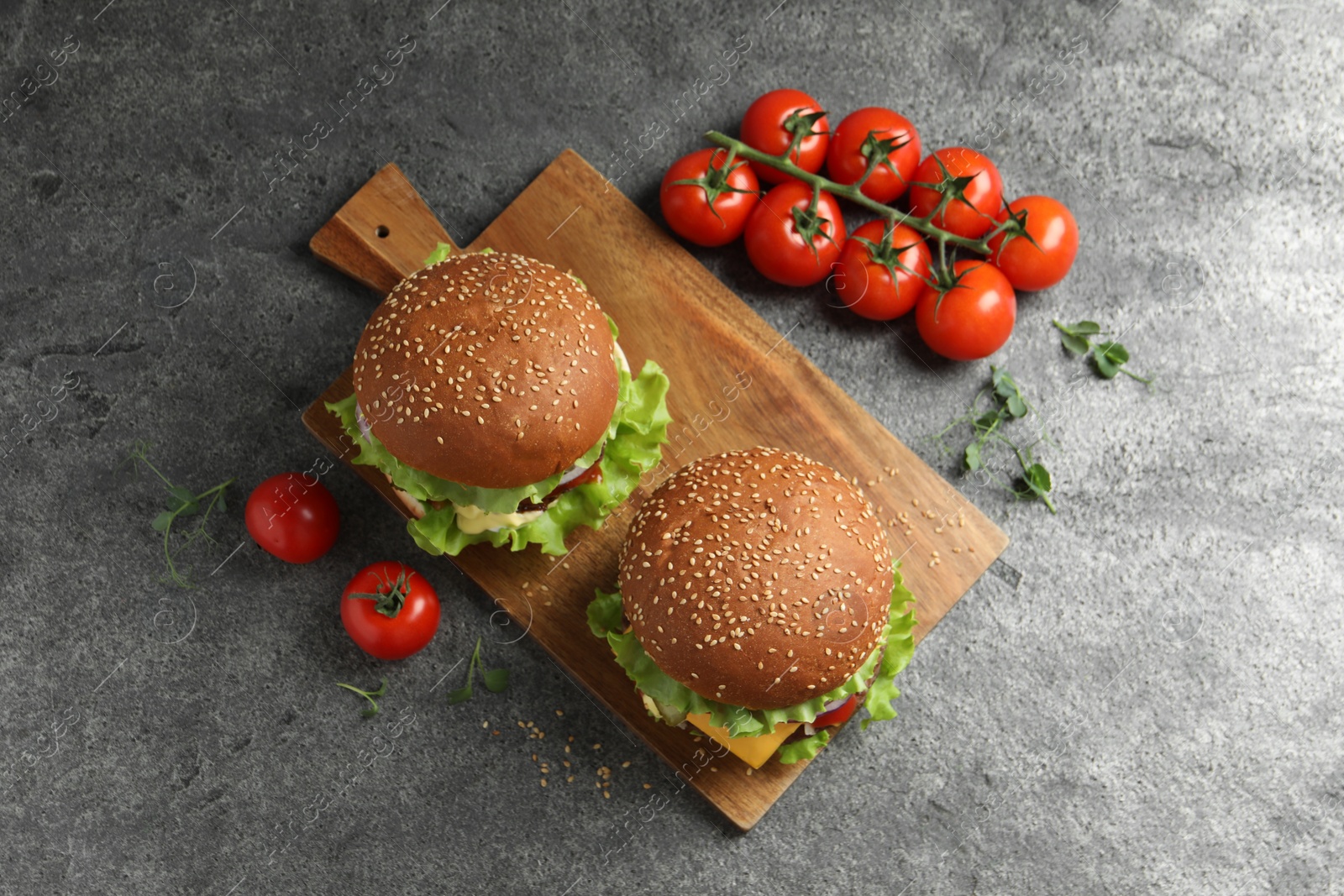 Photo of Delicious burgers with beef patty and tomatoes on grey table, flat lay