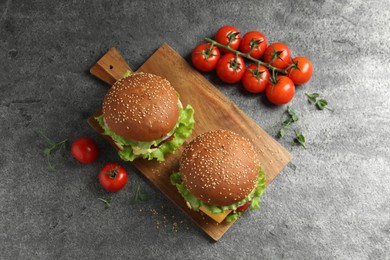 Photo of Delicious burgers with beef patty and tomatoes on grey table, flat lay