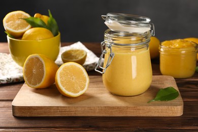 Delicious lemon curd in glass jars, fresh citrus fruits and green leaves on wooden table