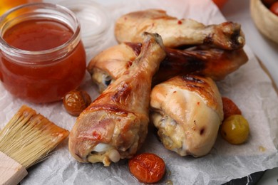 Photo of Marinade, basting brush, roasted chicken drumsticks and tomatoes on table, closeup