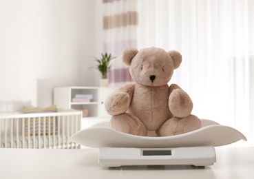 Baby scales with teddy bear on table indoors, space for text