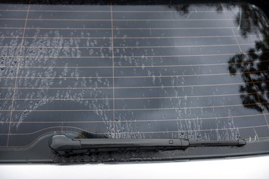 Photo of Wiper cleaning raindrops from car rear windshield outdoors