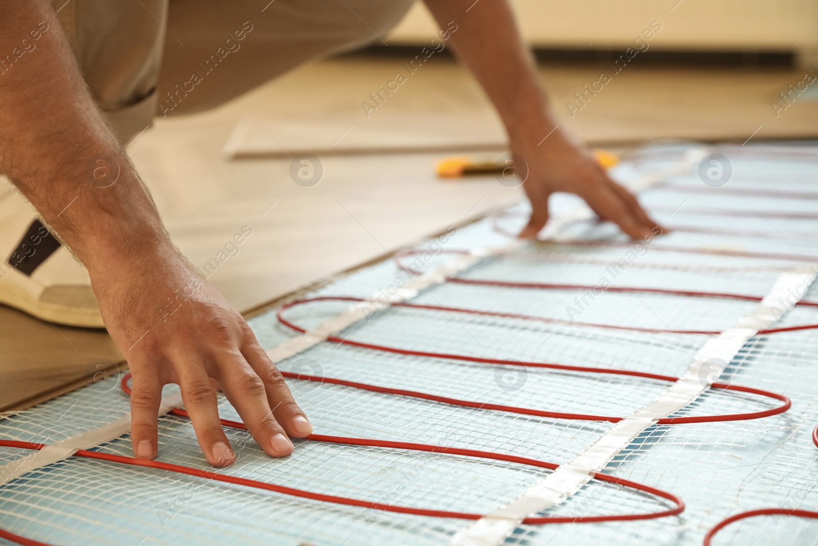 Photo of Professional worker installing electric underfloor heating system indoors, closeup