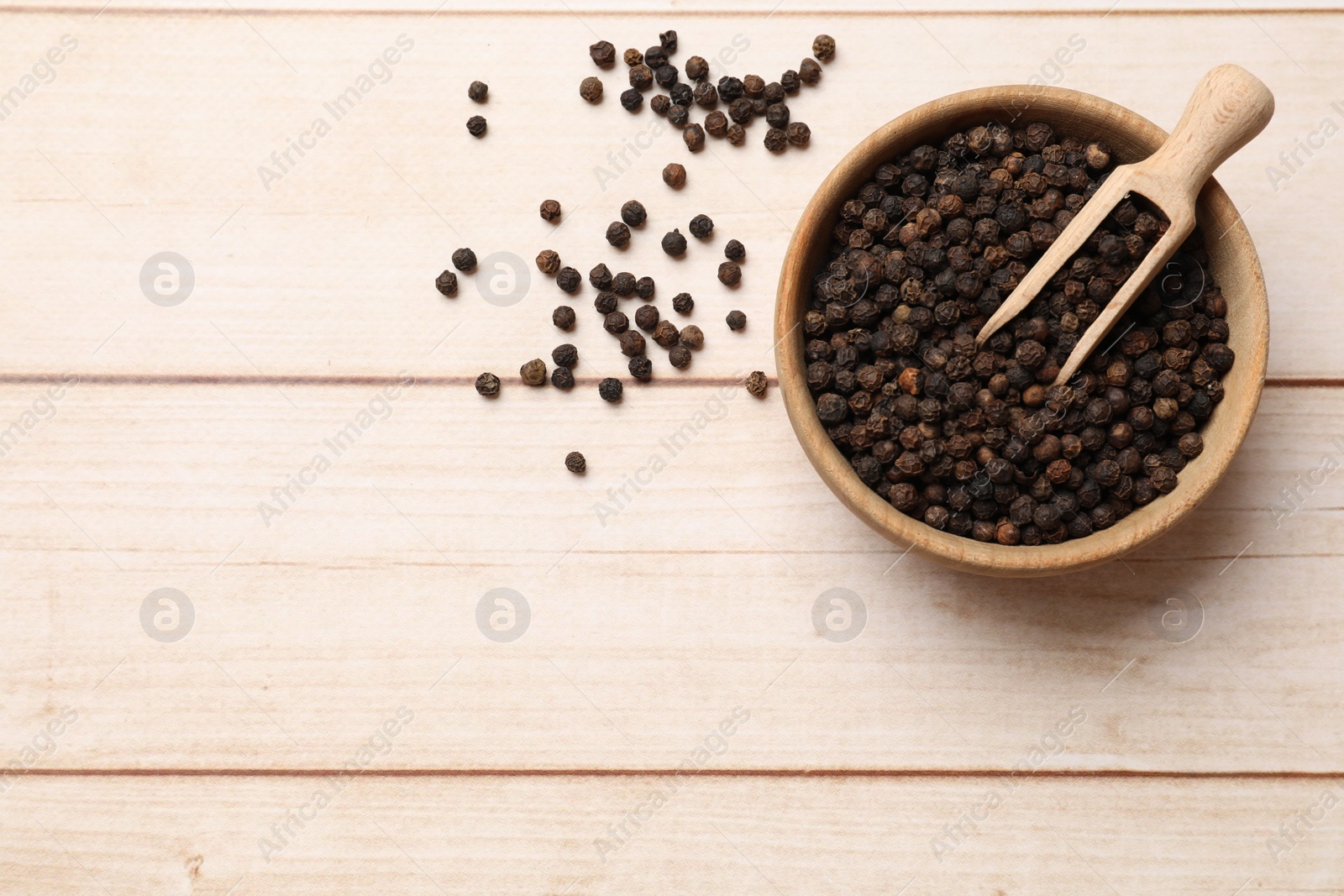 Photo of Aromatic spice. Black peppercorns and scoop in bowl on wooden table, top view. Space for text