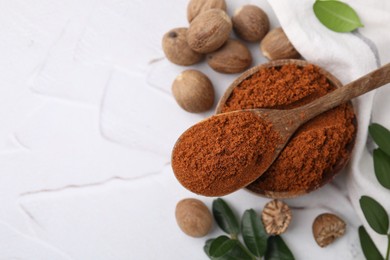 Photo of Nutmeg powder, seeds and green branches on white table, flat lay. Space for text