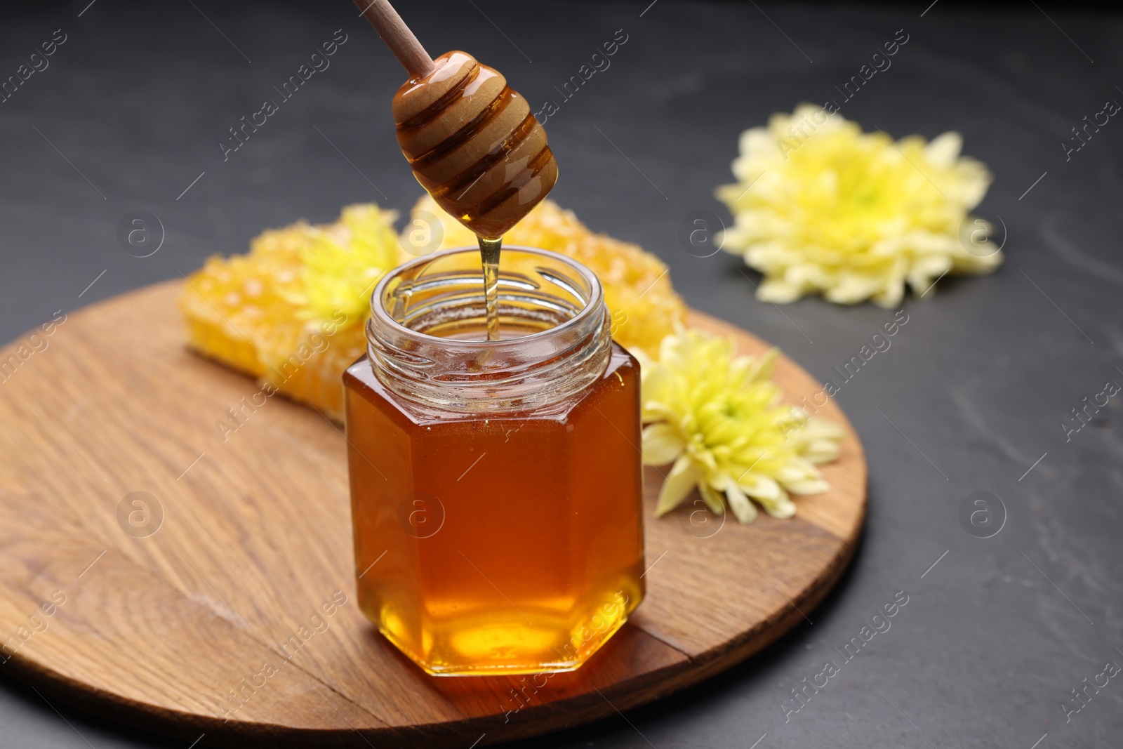 Photo of Pouring sweet honey from dipper into jar at grey table, space for text