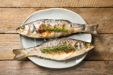 Photo of Delicious baked fish and rosemary on wooden table, top view