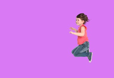 Cute girl jumping on violet background, space for text