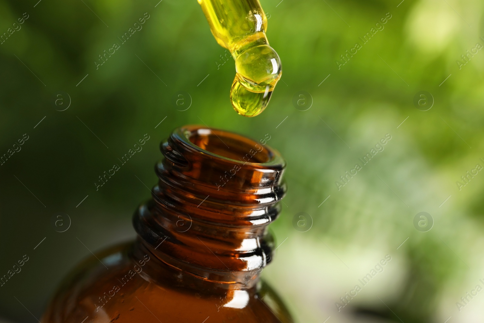 Photo of Pipette with oil over bottle on blurred background. Space for text