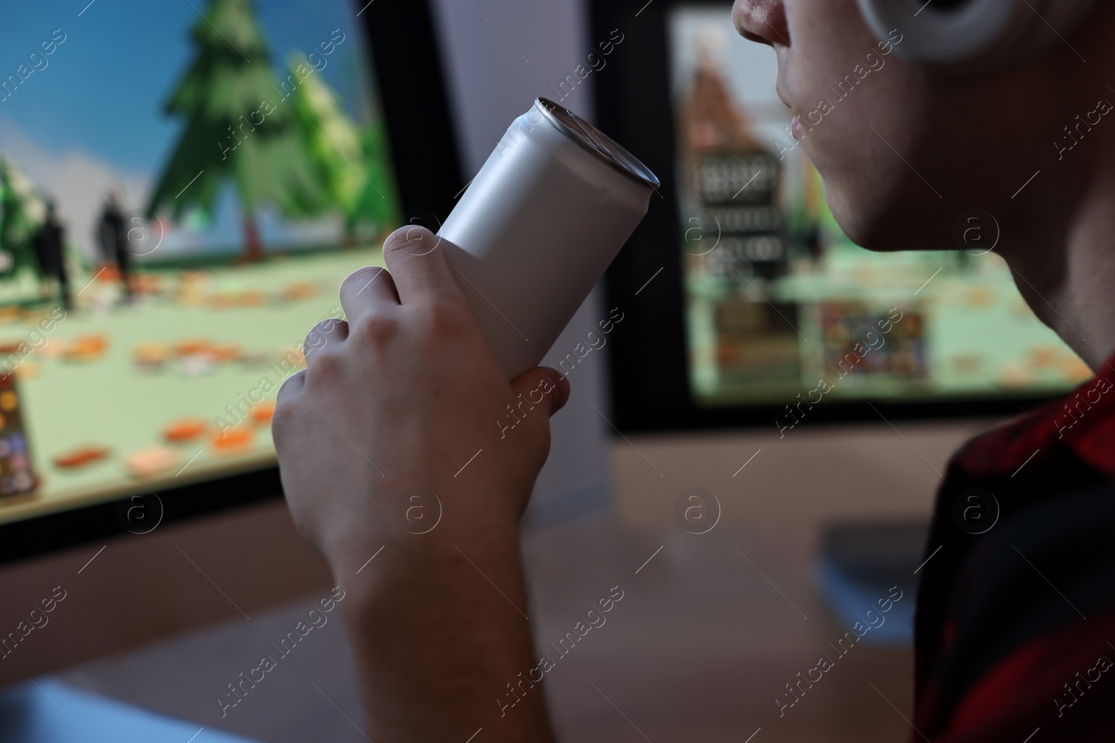 Photo of Young man with energy drink and headphones playing video game at wooden desk indoors, closeup