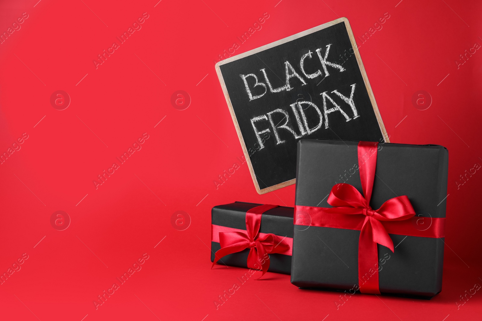 Photo of Gift boxes and chalkboard with words Black Friday on red background, space for text