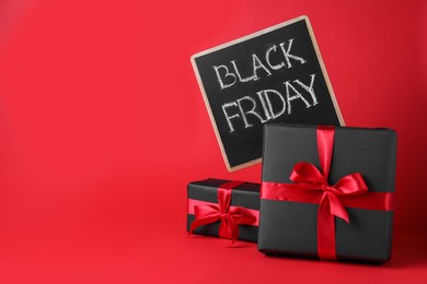 Gift boxes and chalkboard with words Black Friday on red background, space for text