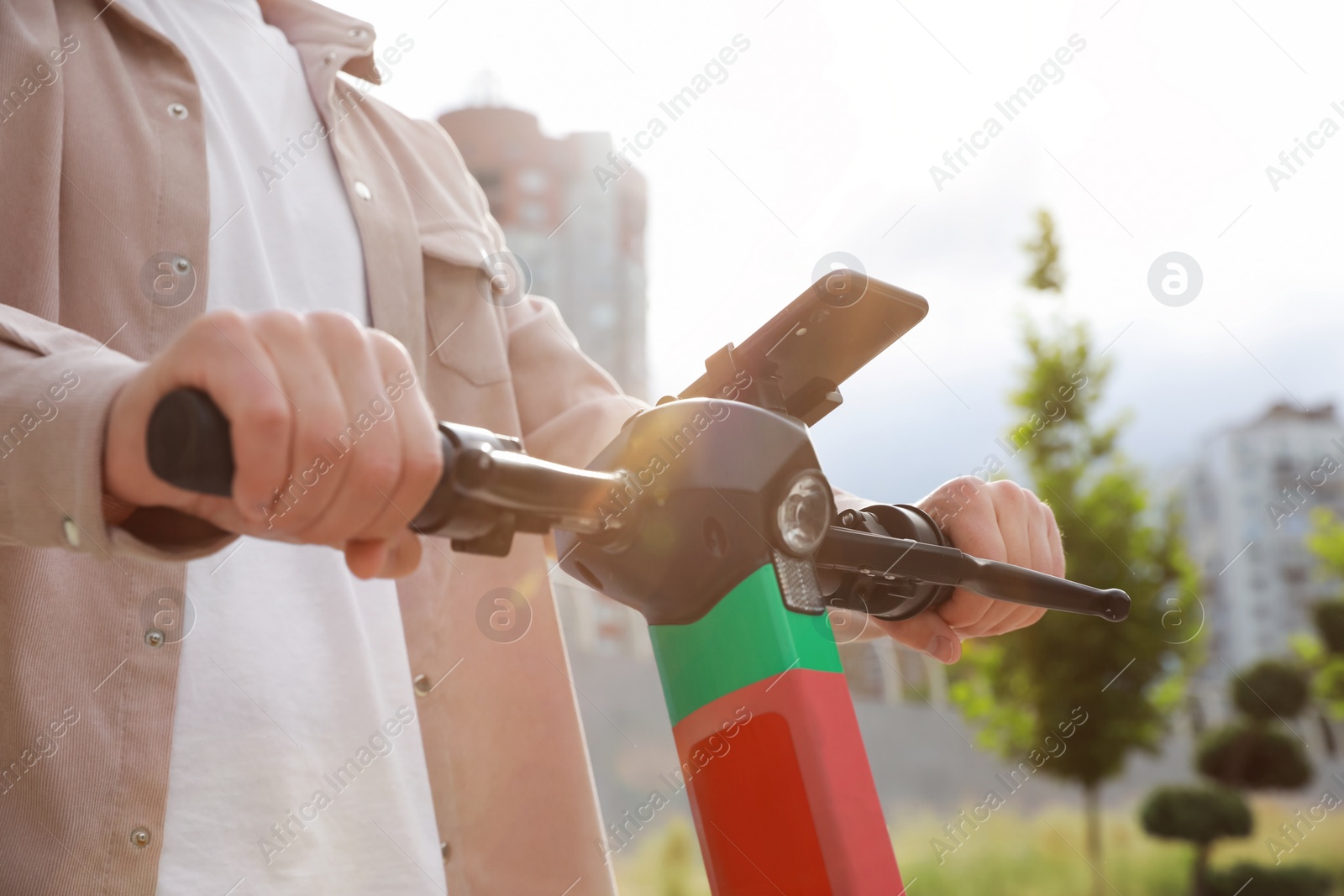 Photo of Man riding modern electric kick scooter with smartphone outdoors, closeup