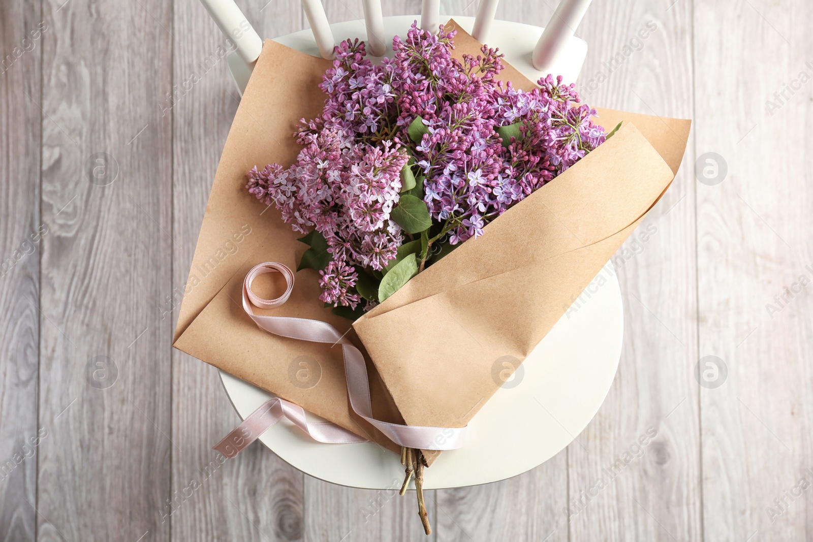 Photo of Beautiful blossoming lilac on chair indoors, top view. Spring flowers