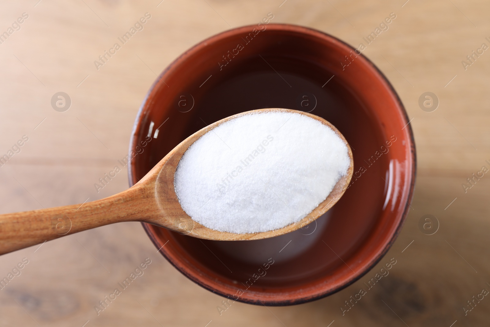 Photo of Spoon with baking soda over glass of water on wooden table, top view