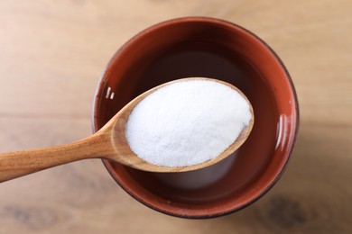 Spoon with baking soda over glass of water on wooden table, top view