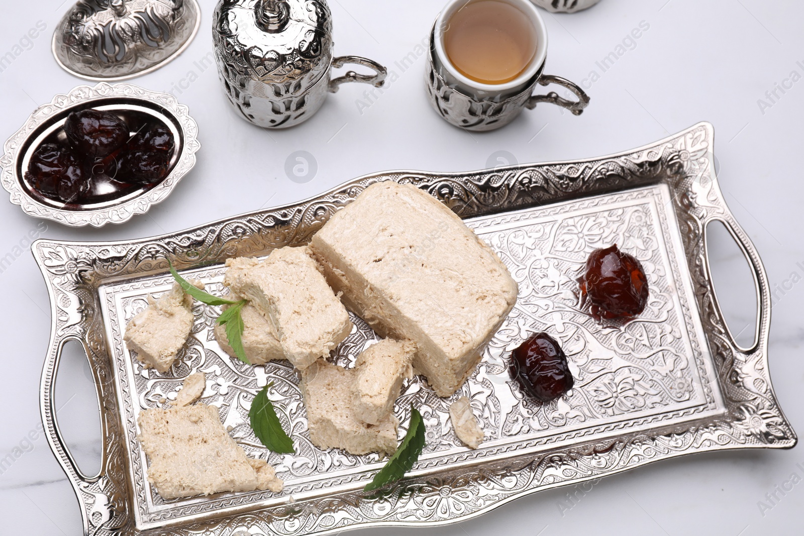 Photo of Pieces of tasty halva, tea, dates and mint leaves on white marble table, above view