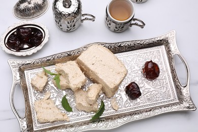 Pieces of tasty halva, tea, dates and mint leaves on white marble table, above view