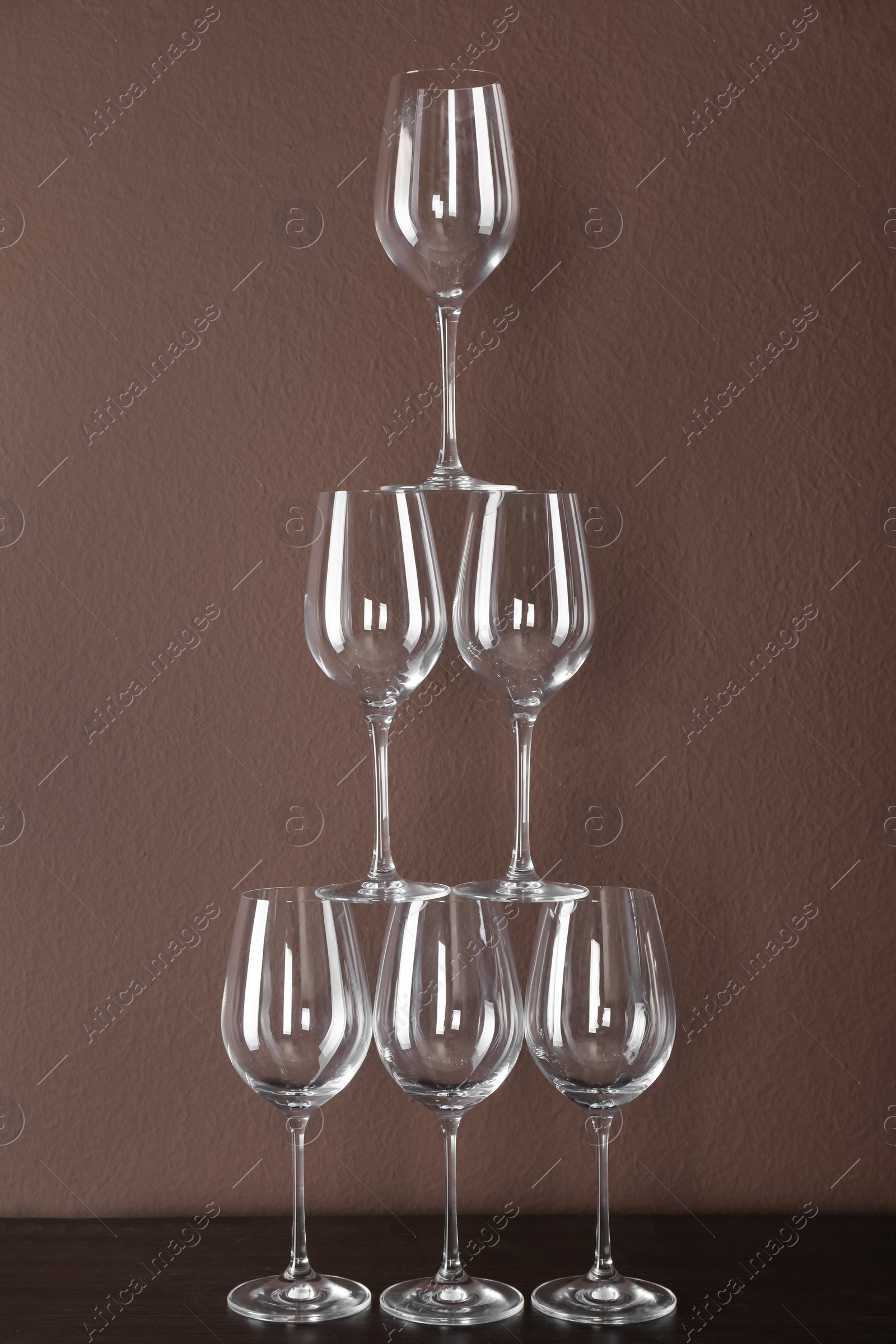 Photo of Tower made of wine glasses on wooden table near brown wall