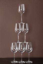 Photo of Tower made of wine glasses on wooden table near brown wall