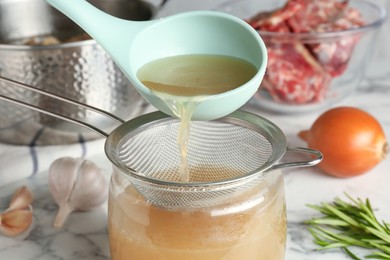 Photo of Straining delicious broth through sieve on white marble table, closeup