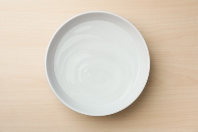 White bowl with water on wooden table, top view
