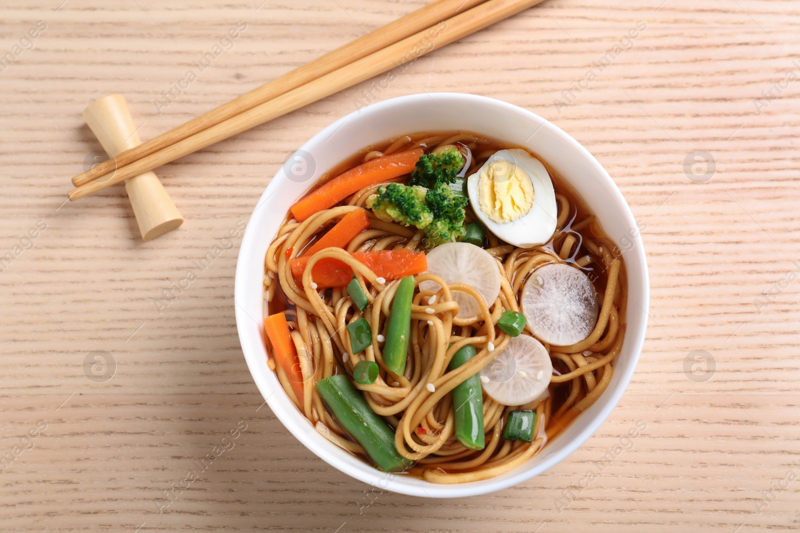 Photo of Tasty ramen with noodles, vegetables and chopsticks on wooden table, top view