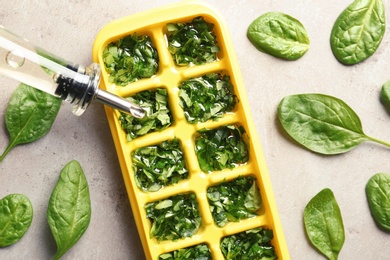 Photo of Pouring oil into ice cube tray with spinach on grey background, top view