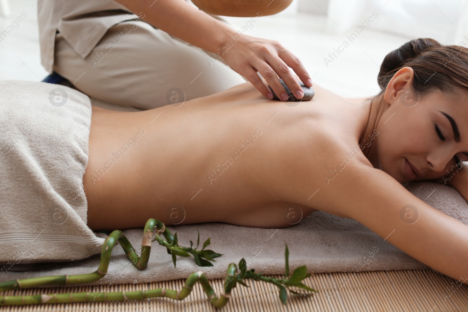 Photo of Beautiful young woman getting hot stone massage in spa salon