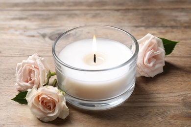 Beautiful roses near candle in glass holder on wooden table