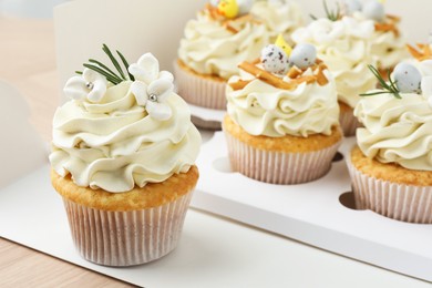 Photo of Tasty Easter cupcakes in box on wooden table, closeup