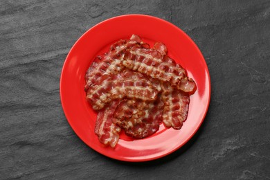 Plate with fried bacon slices on dark textured table, top view