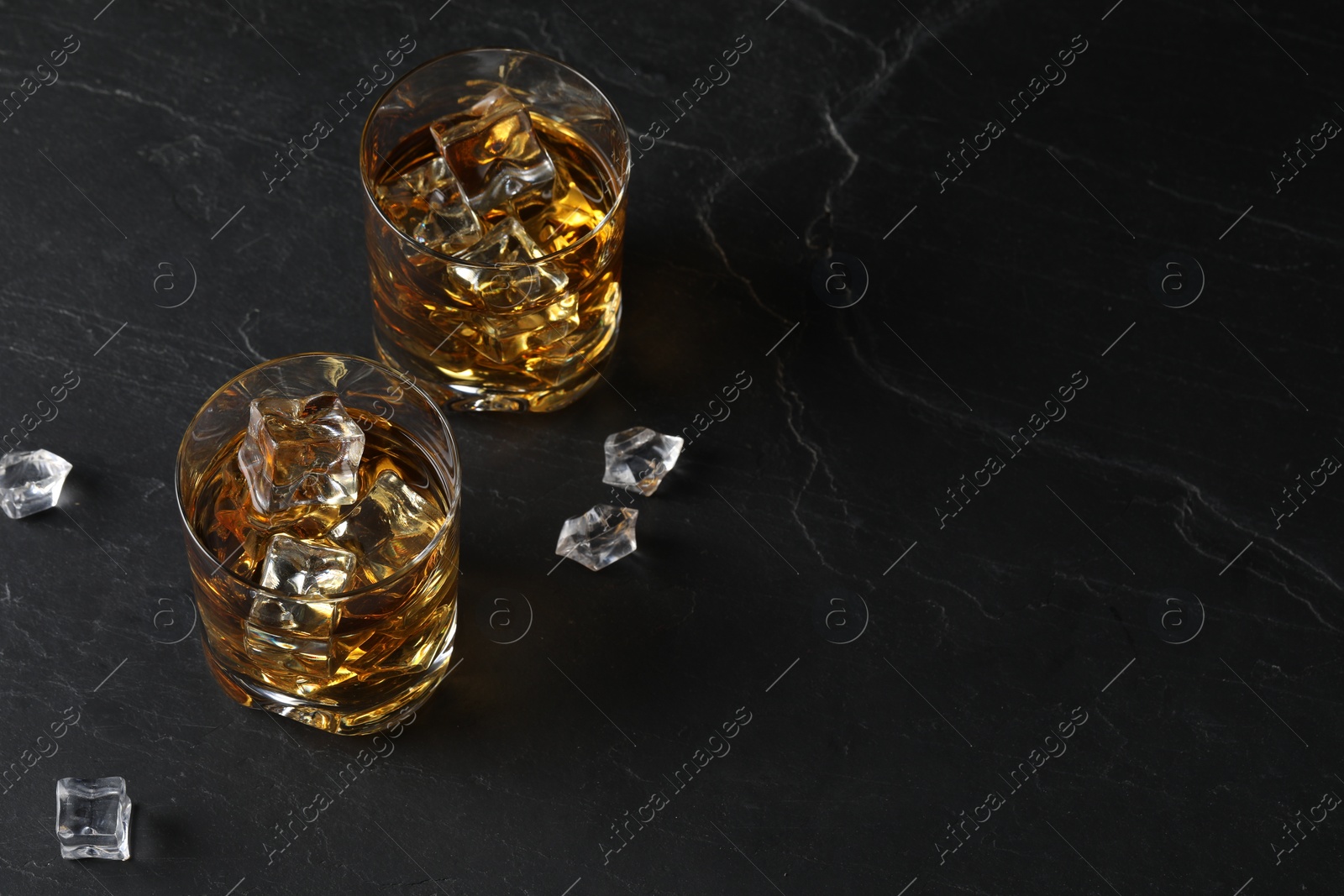 Photo of Whiskey and ice cubes in glasses on black table, above view. Space for text