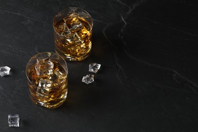 Whiskey and ice cubes in glasses on black table, above view. Space for text