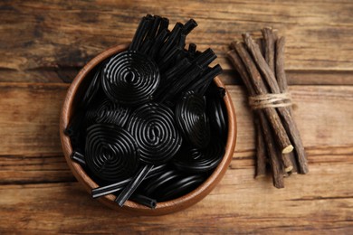 Tasty black candies and dried sticks of liquorice root on wooden table, flat lay