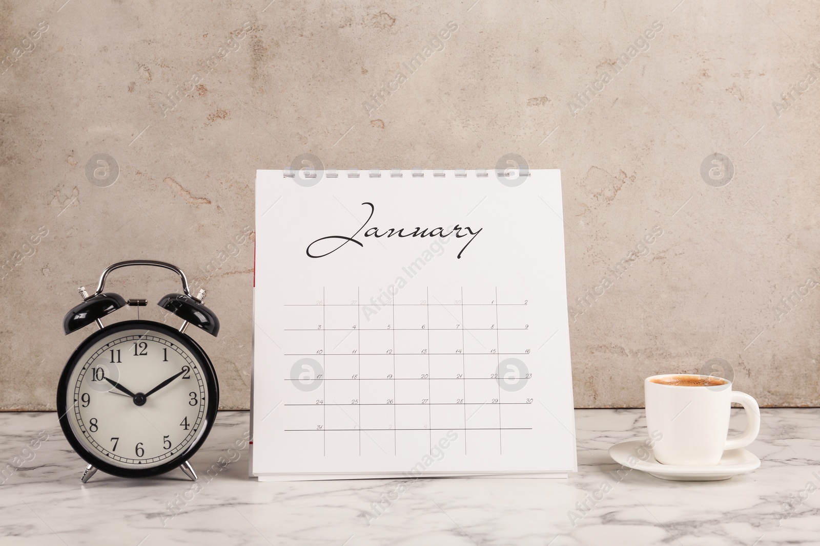 Photo of Calendar, alarm clock and cup of coffee on marble table