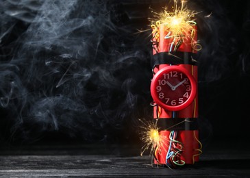 Image of Dynamite time bomb with burning wires on black wooden table, space for text