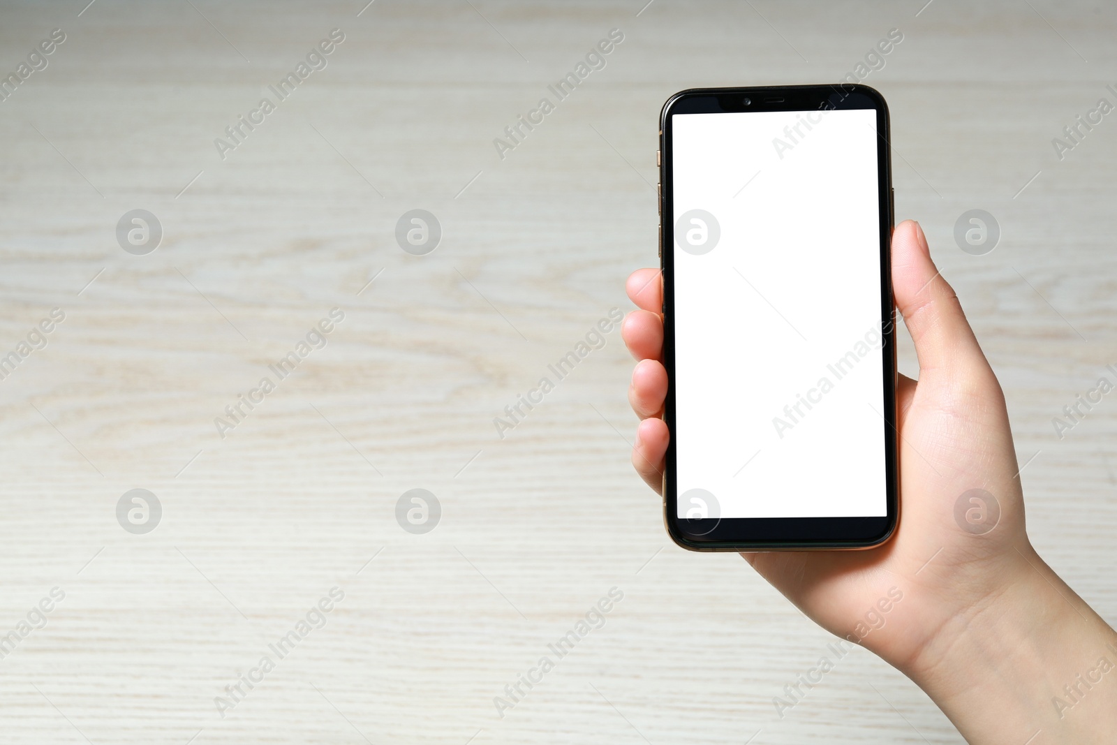 Photo of Woman holding smartphone with blank screen at white wooden table, top view. Mockup for design