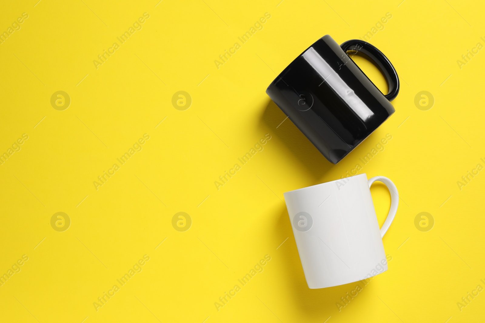 Black and white ceramic mugs on yellow background, flat lay. Space for text Photo of Black and white ceramic mugs on yellow background, flat lay. Space for text