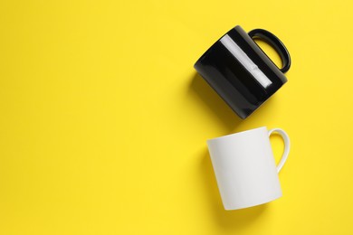 Photo of Black and white ceramic mugs on yellow background, flat lay. Space for text