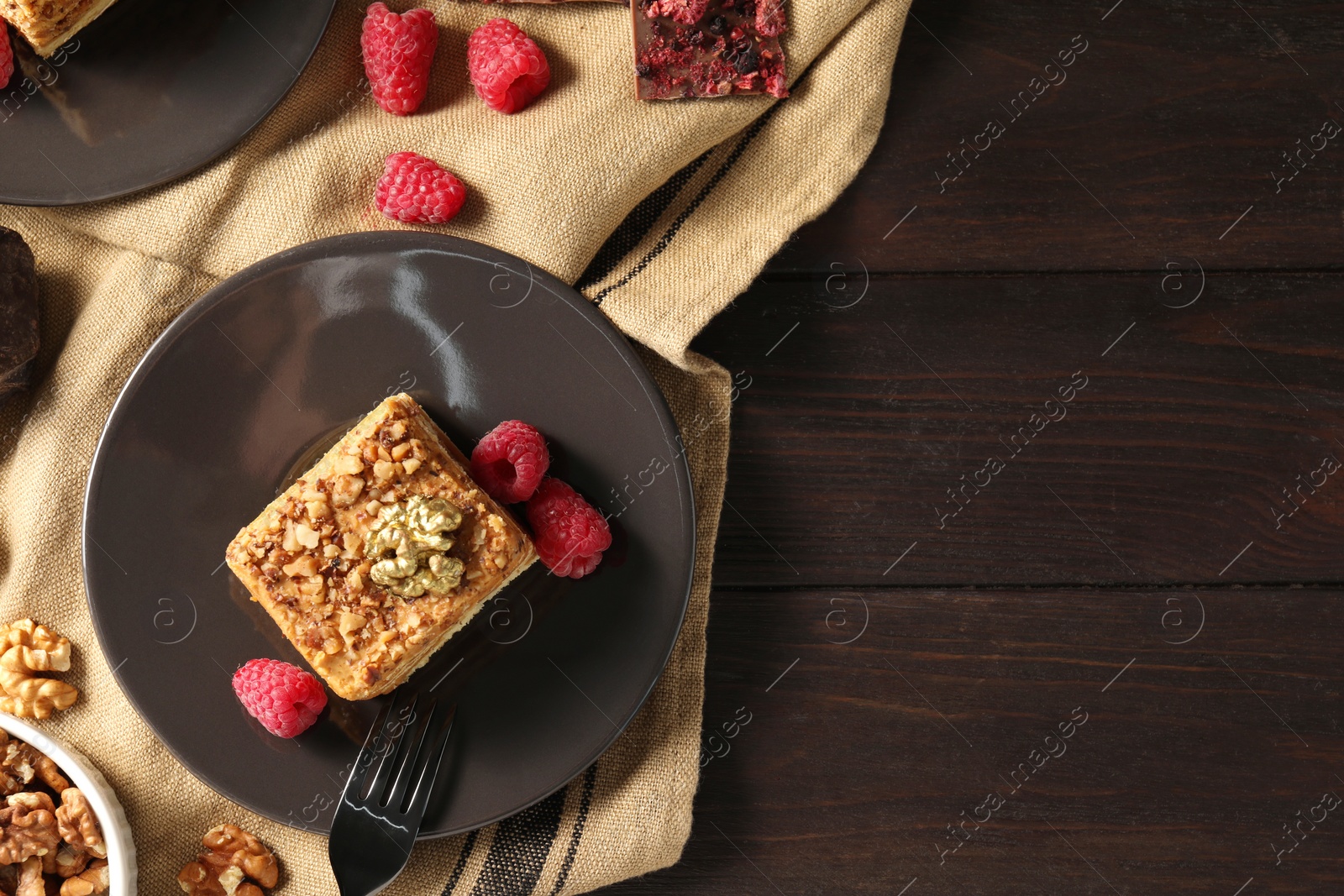Photo of Piece of delicious layered honey cake with raspberries served on wooden table, flat lay. Space for text