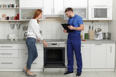 Photo of Housewife with repairman near modern oven in kitchen